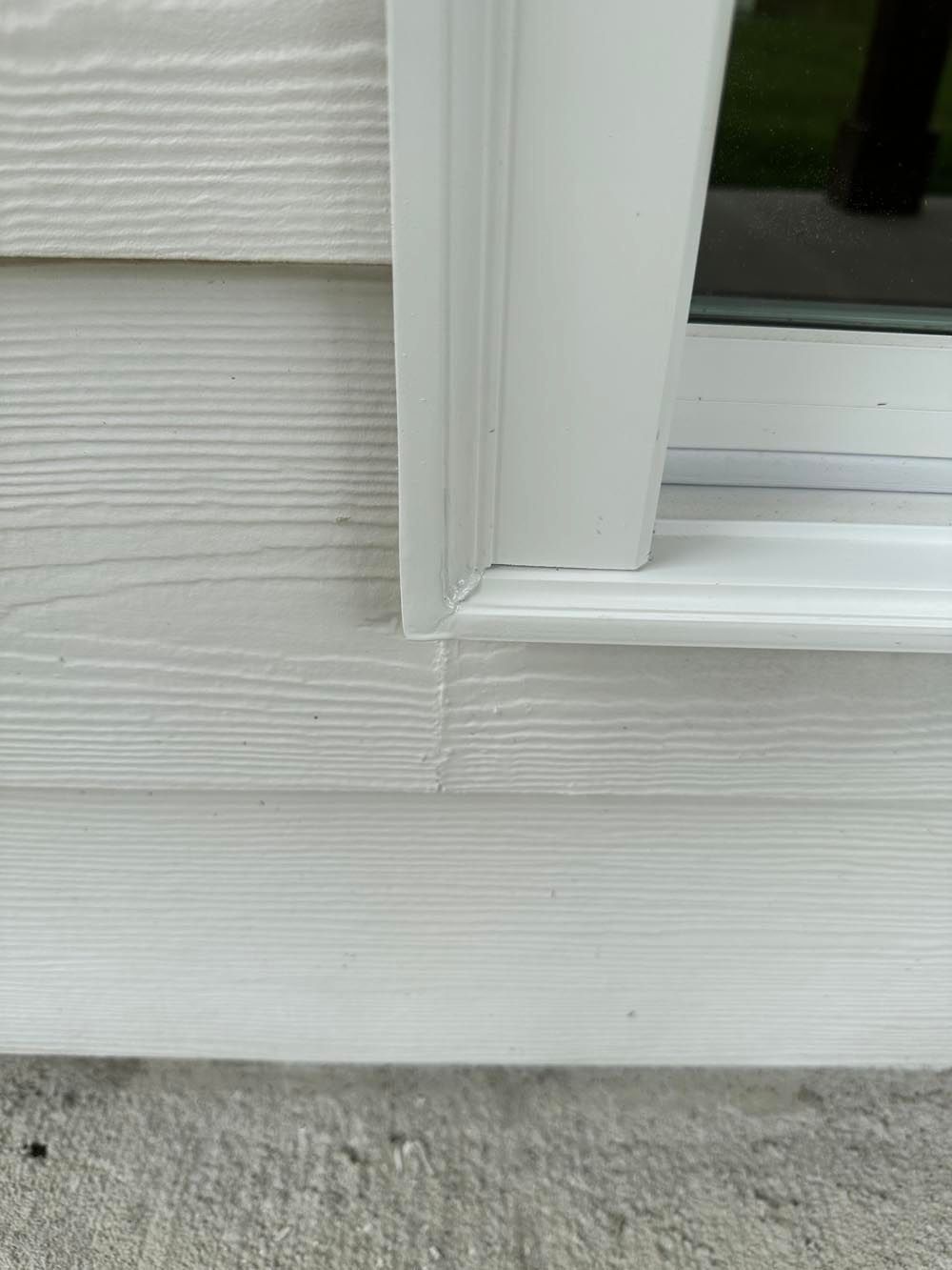 White vinyl siding and window trim meet; a concrete ledge is at the bottom.