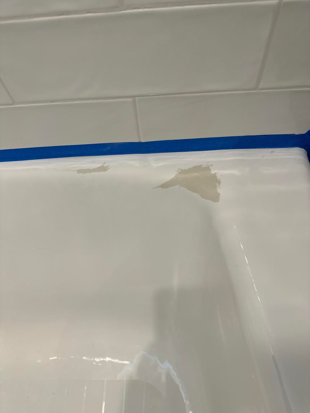 White bathtub with peeling paint, blue tape at the top, white tiled wall in background.