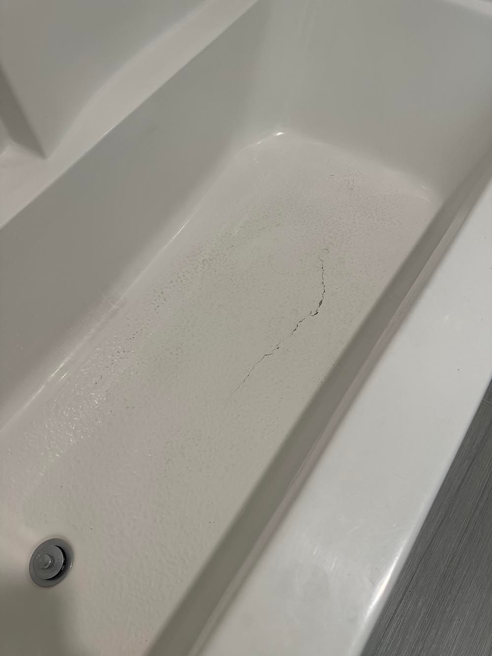 White bathtub with a drain, containing small dark marks and some water.