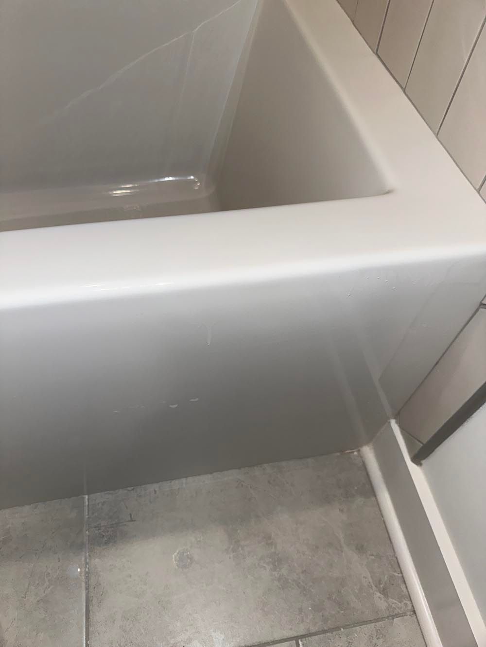 White bathtub with a square edge, next to tiled wall and flooring.