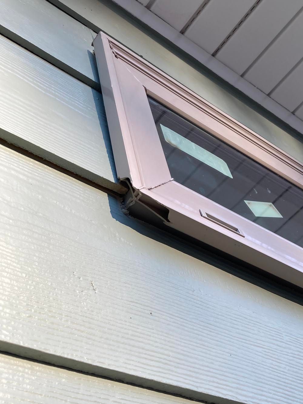 Close-up of a window frame angled against blue siding; the frame is white, and part of the hinge is visible.