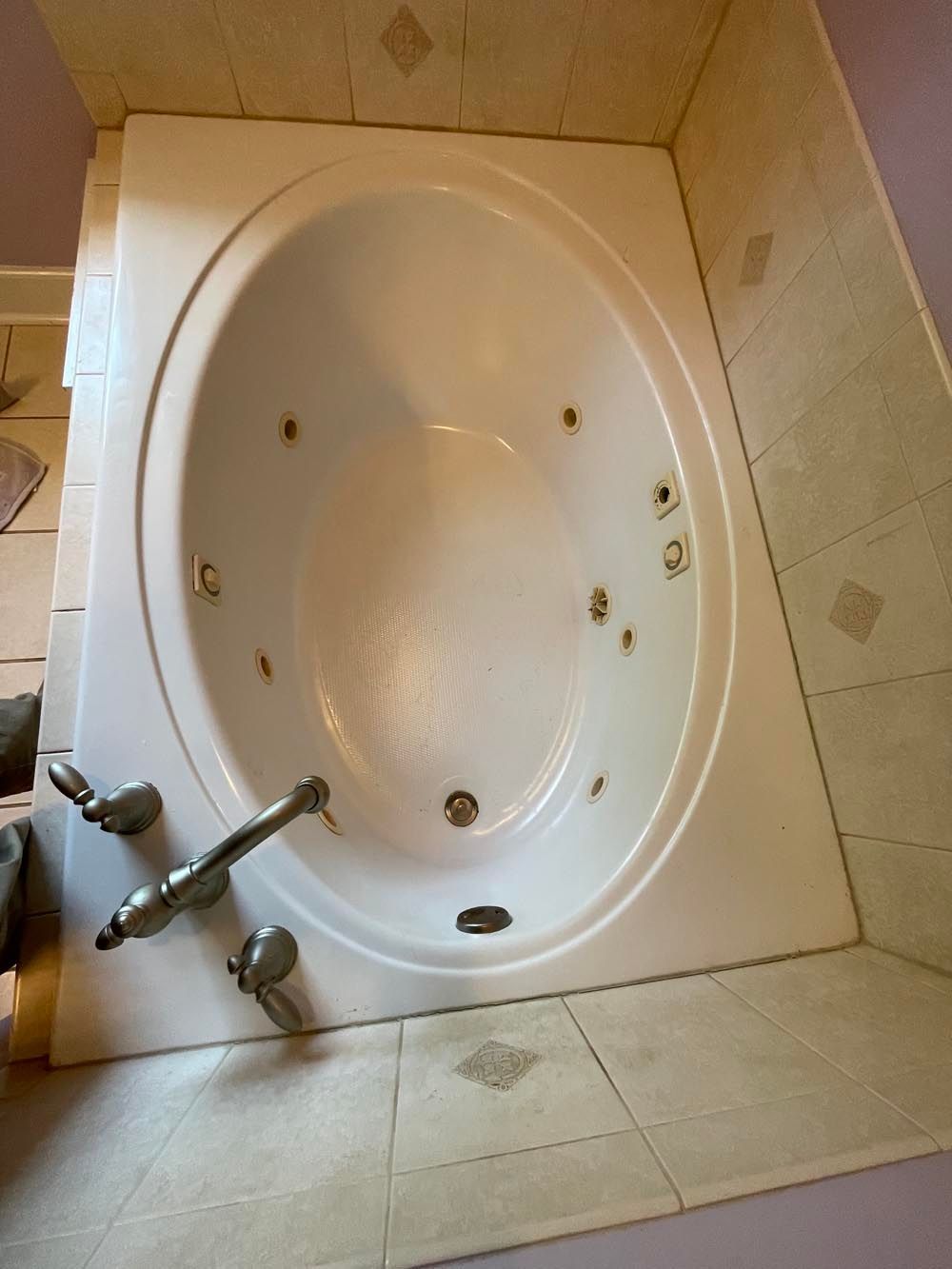Oval jacuzzi tub surrounded by light-colored tile and chrome fixtures.