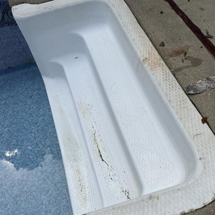 White pool steps with dirt and algae, next to blue pool water and concrete.