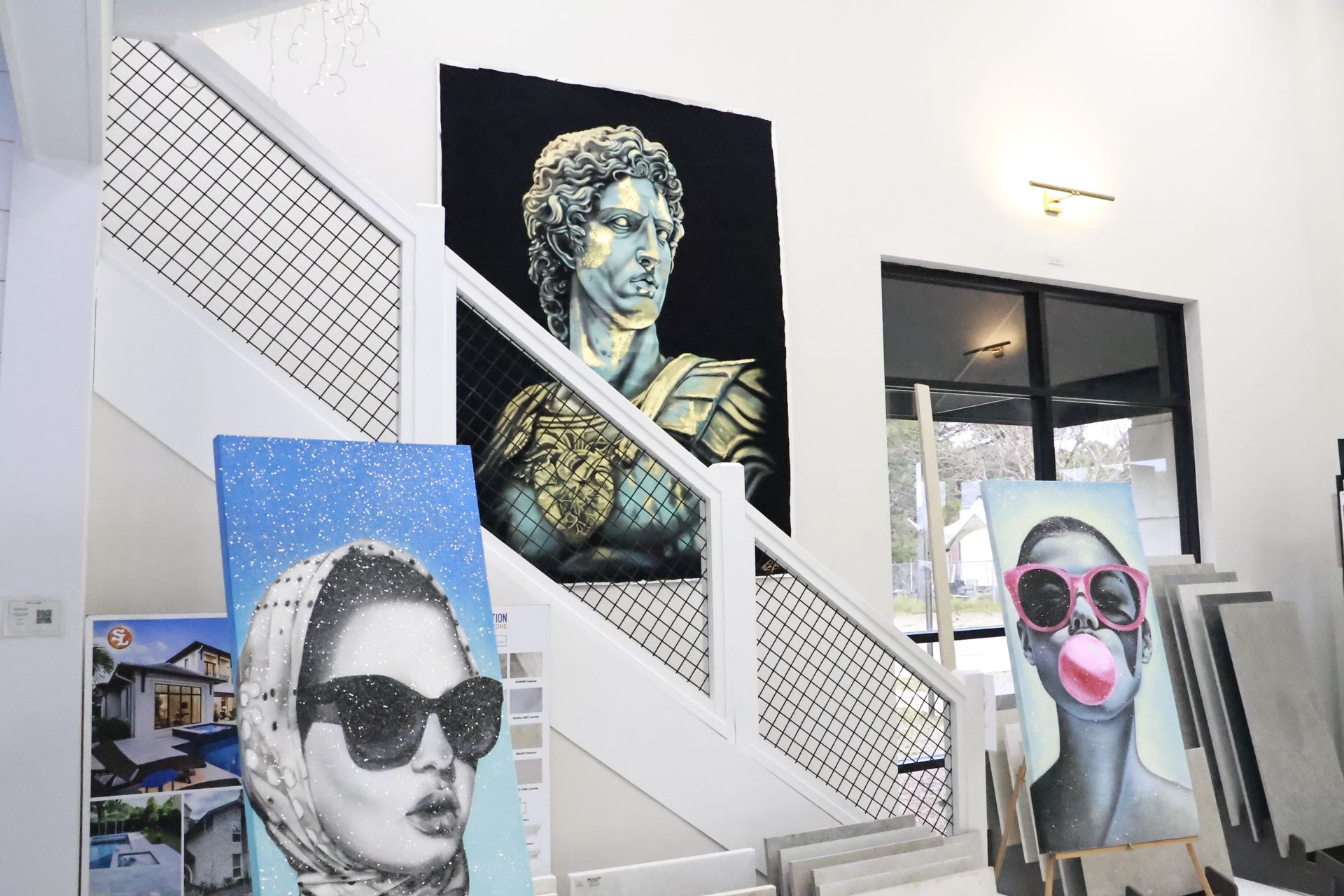 Artwork displayed on walls and stairs of a gallery. Includes a bust, portraits, and a seascape.