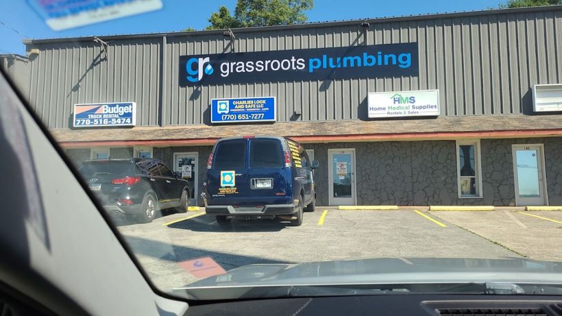 A car is parked in front of a grassroots plumbing building.