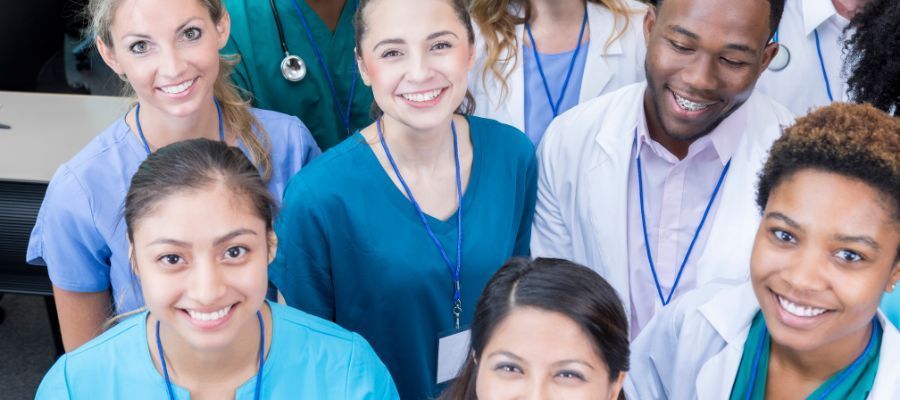 A group of diverse medical professionals smiling at the camera in a clinical setting.