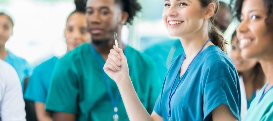 Smiling healthcare professionals in teal scrubs are gathered in a well-lit room.