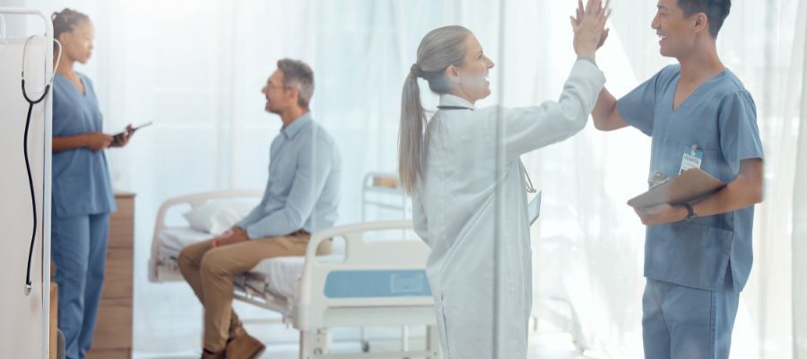 Doctors and nurses high-five. A patient sits in a hospital bed. A nurse holds a clipboard.