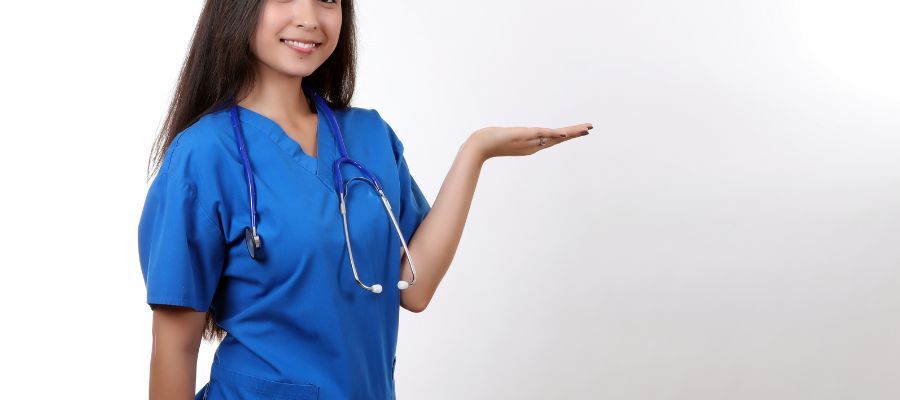 Smiling nurse in blue scrubs with a stethoscope, holds out an open hand, white background.