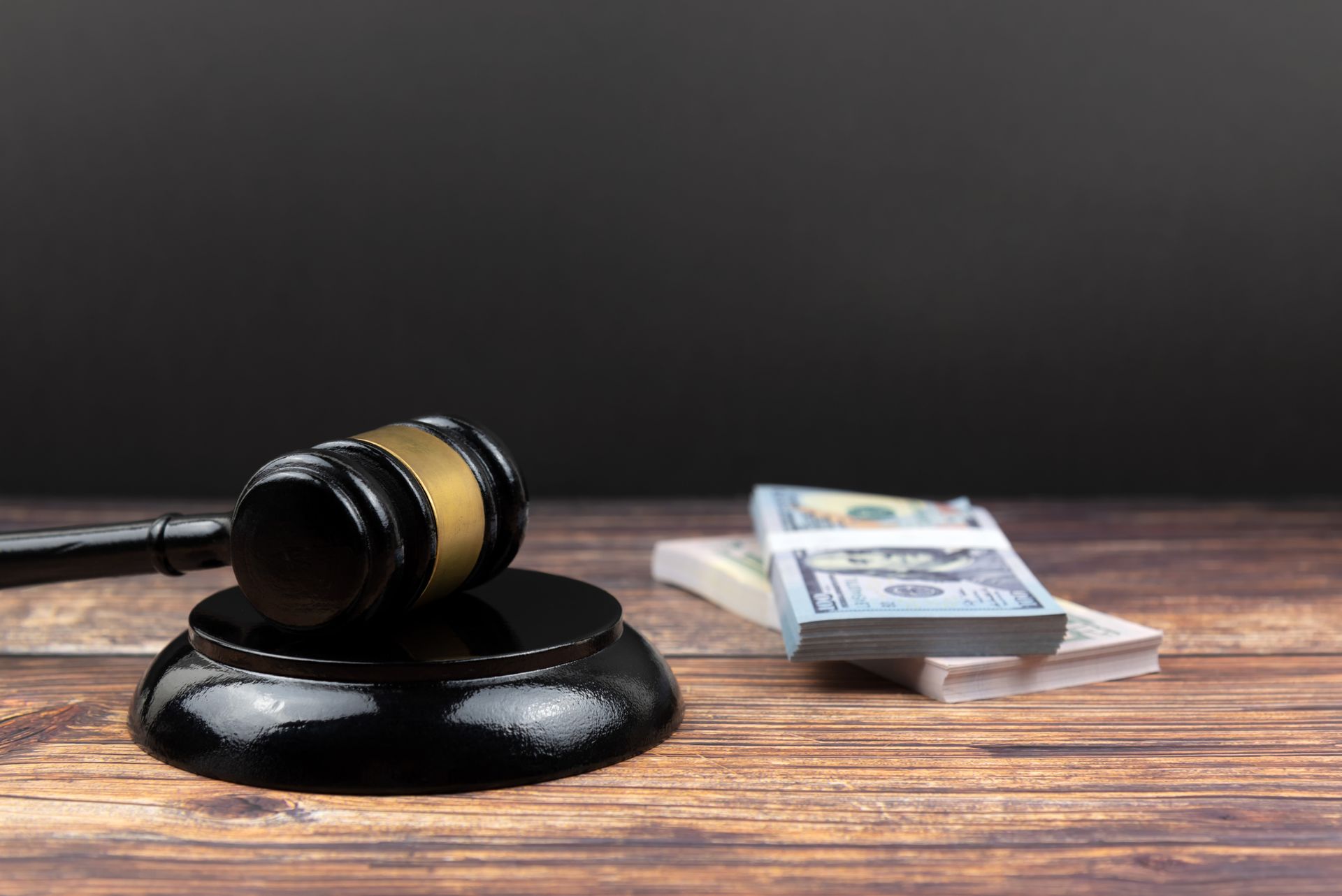 A judge's gavel rests on a wooden table surrounded by stacks of money, symbolizing a bail bondsman.