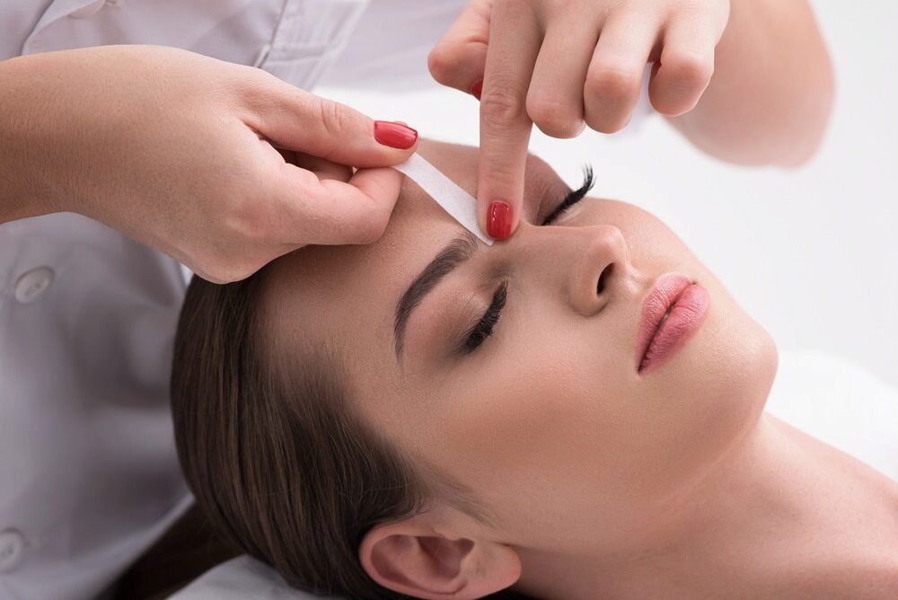 A Woman is Getting Her Eyebrows Waxed in a Beauty Salon — Rayzr Hair Artistry in Eli Waters, QLD