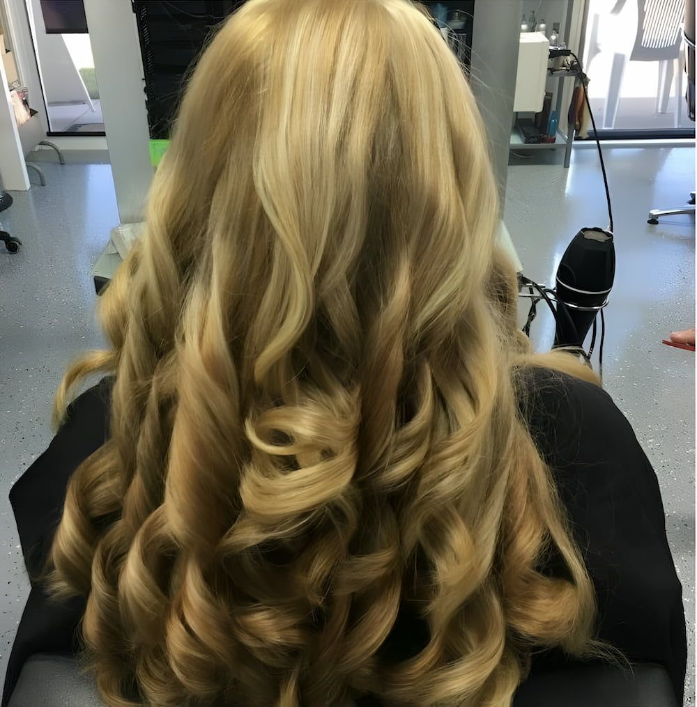 A Woman With Long Blonde Hair is Sitting in a Chair — Rayzr Hair Artistry in Hervey Bay, QLD