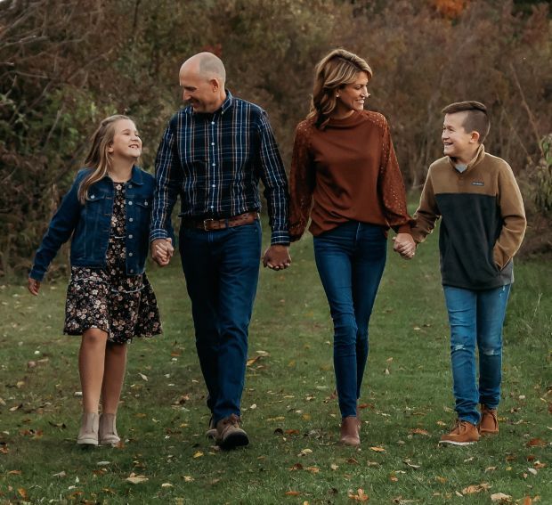A family is walking down a grassy path holding hands.