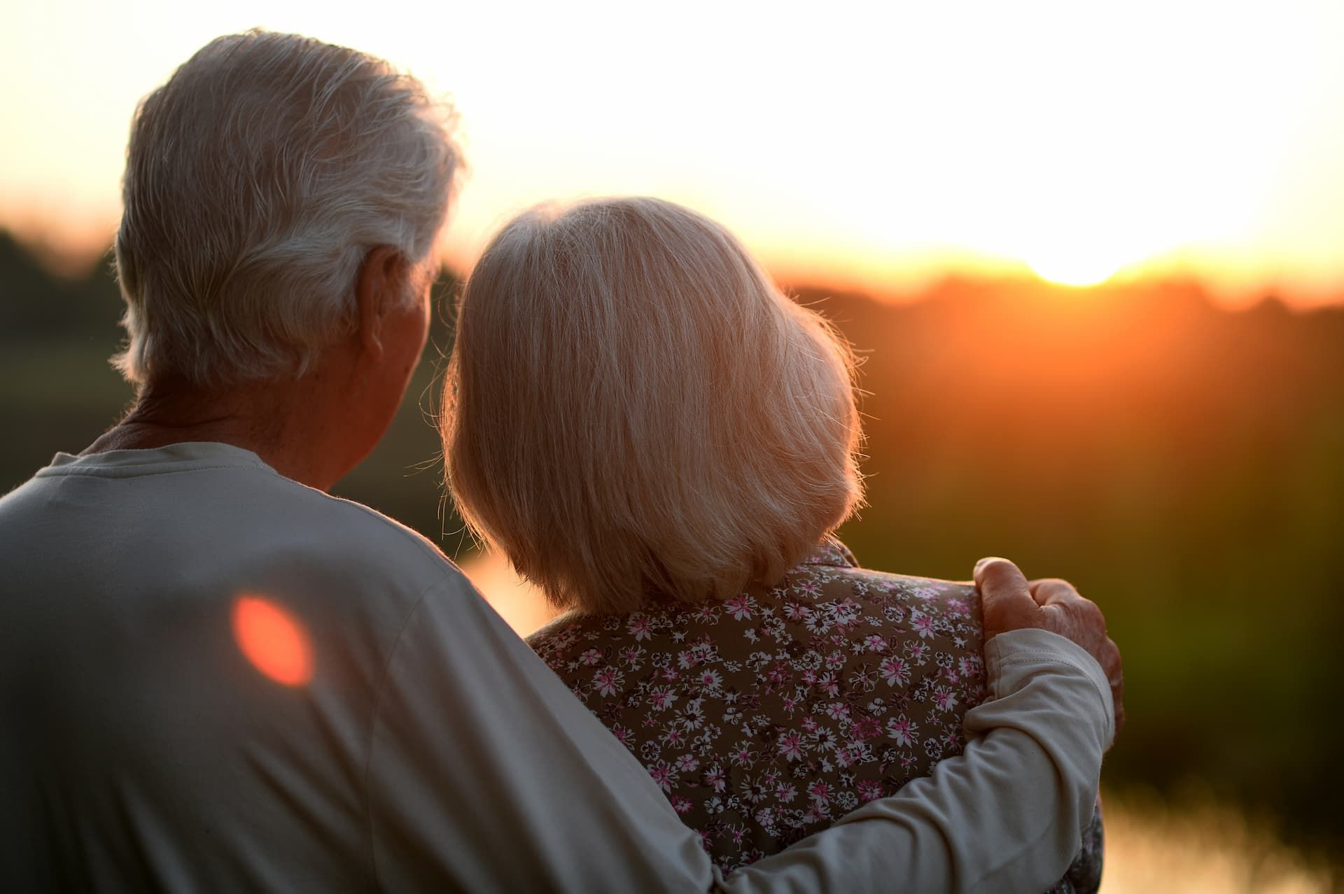 An elderly couple is looking at the sunset over a lake.