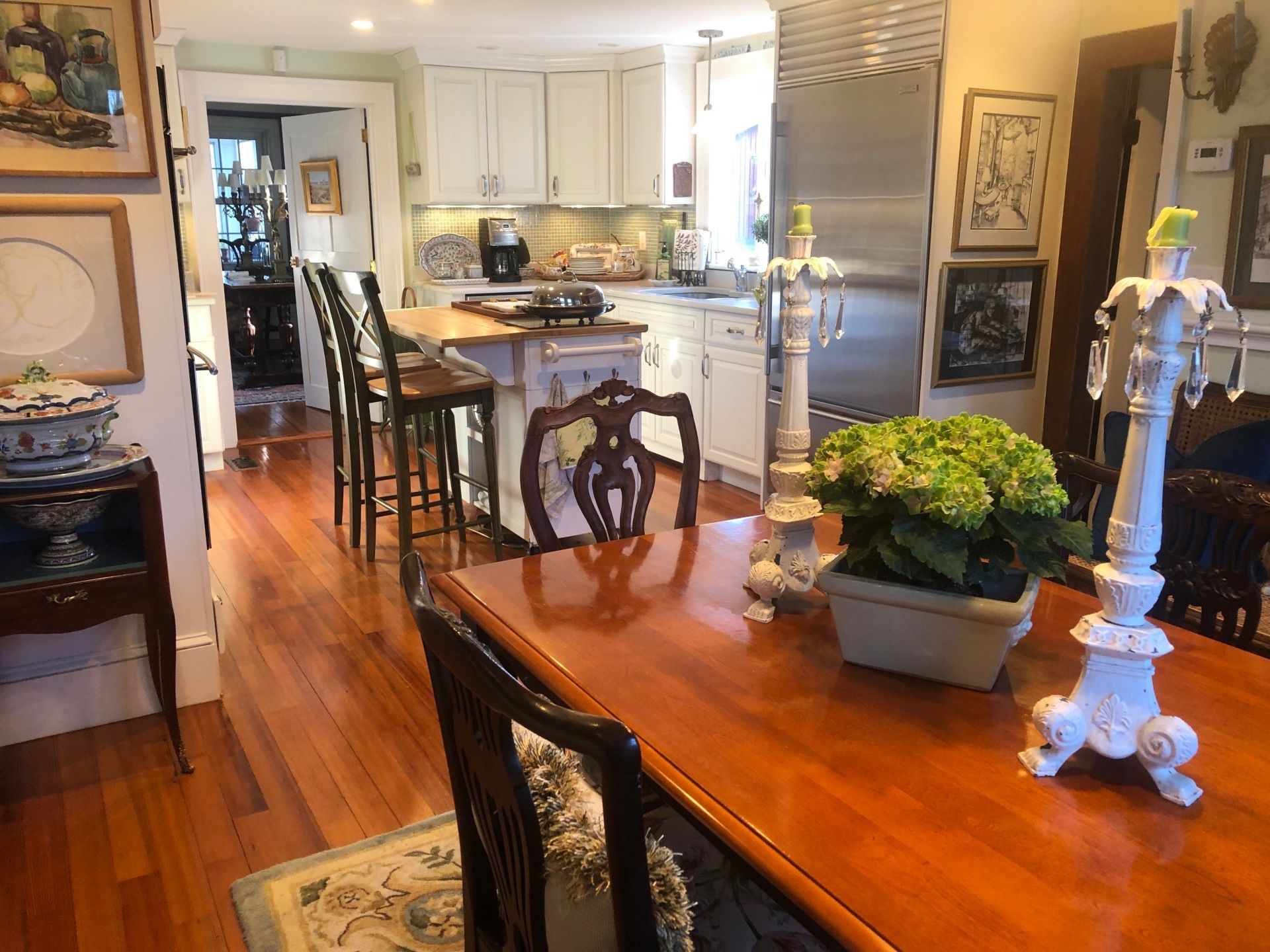 Wooden dining table with ornate chairs, leading to a kitchen with white cabinets and a center island.