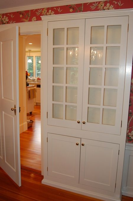 A white cabinet with glass doors is open to a kitchen