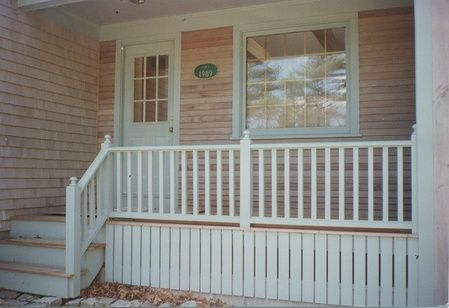 The front porch of a house with a white railing and stairs