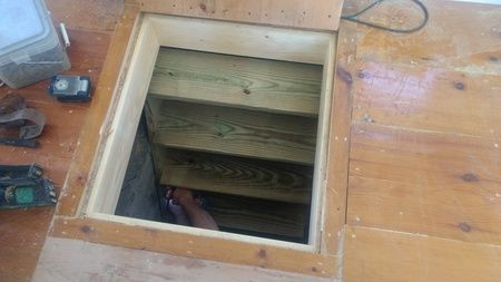 A person is standing in a hole in the floor next to a wooden staircase.