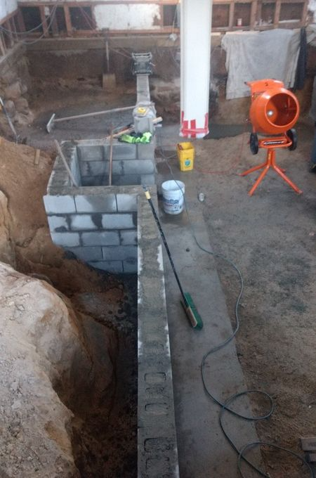 A brick wall is being built in a basement next to a cement mixer.
