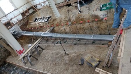A construction site with a ladder and a shovel in the dirt.