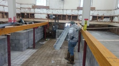 A man is carrying a metal beam in a building under construction.