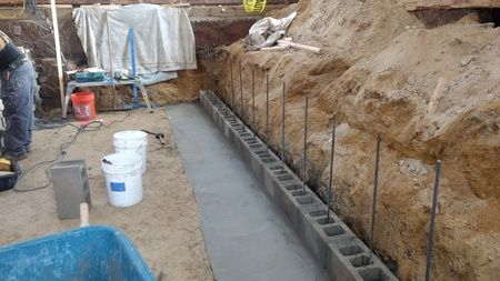 A man is working on a concrete wall in a dirt area.