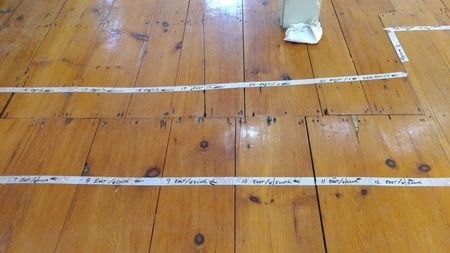 A person is standing on a wooden floor with a white line drawn on it.
