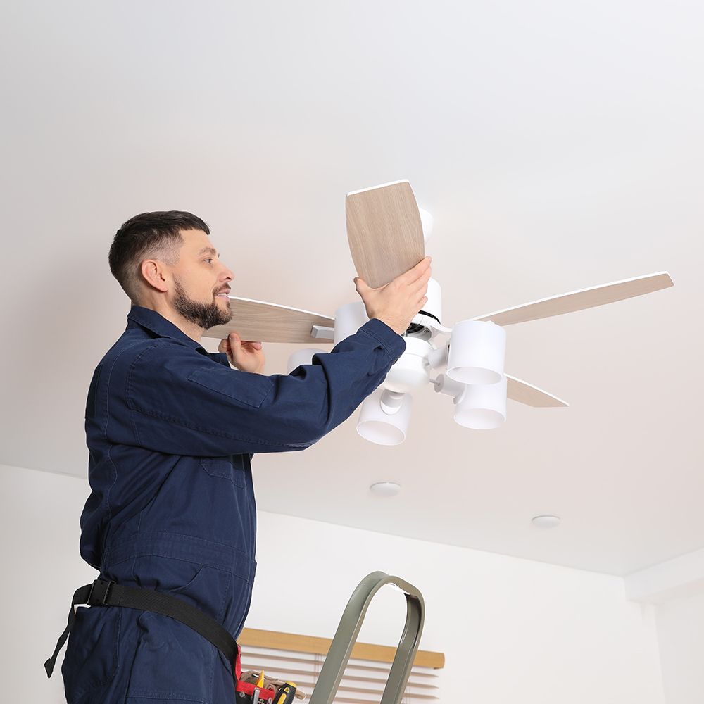 A man is installing a ceiling fan in a living room.