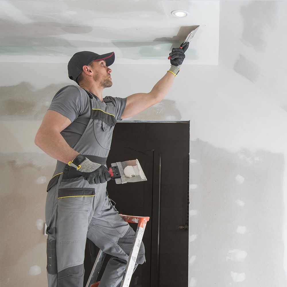 A man is standing on a ladder painting the ceiling.