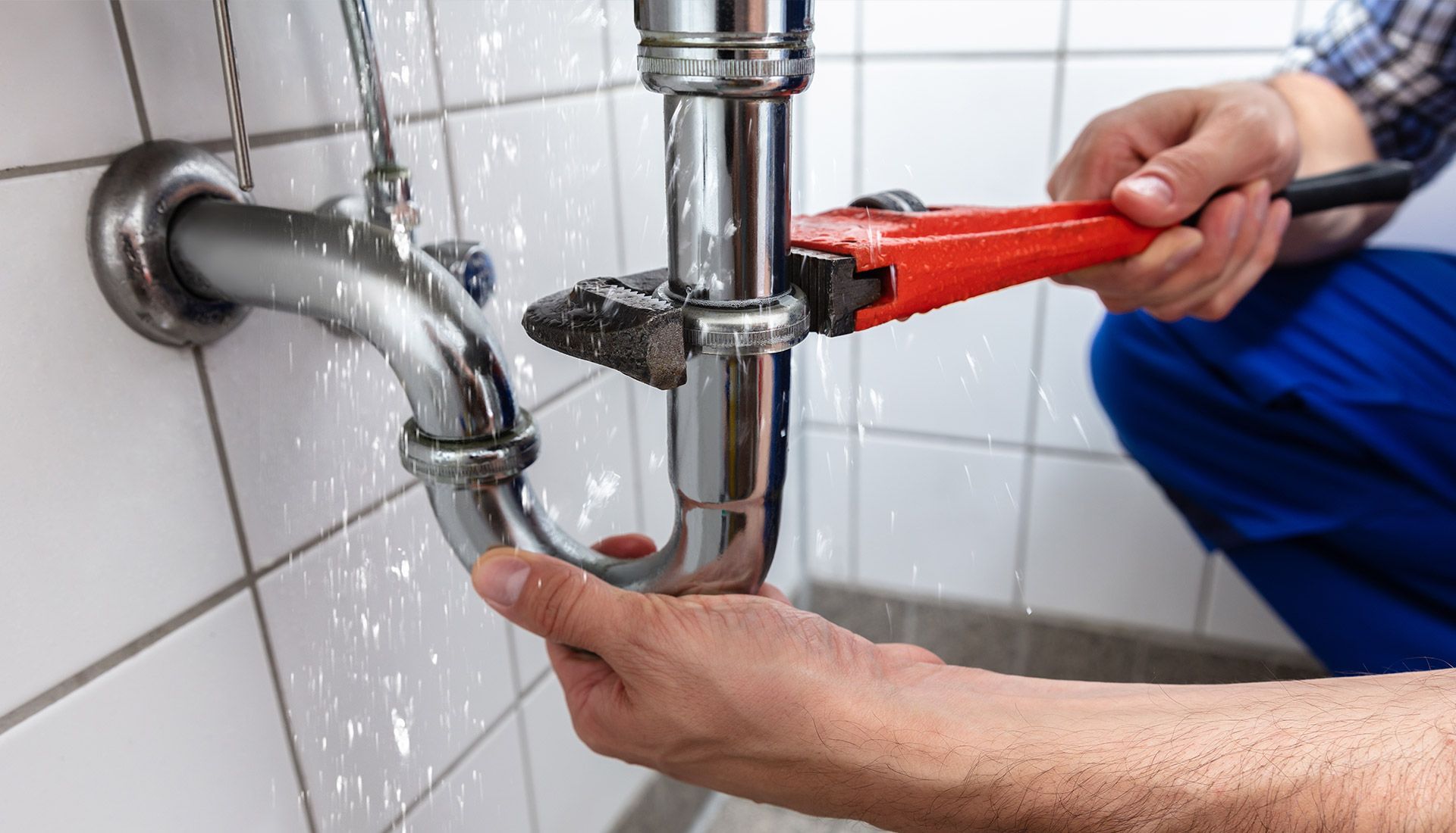 A plumber is fixing a pipe in a bathroom with a wrench.