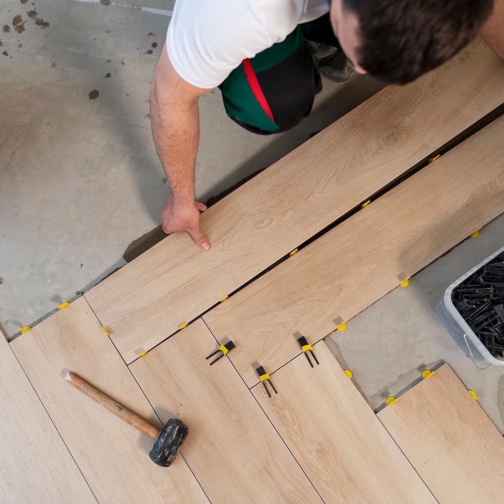 A man is installing a wooden floor with a hammer.