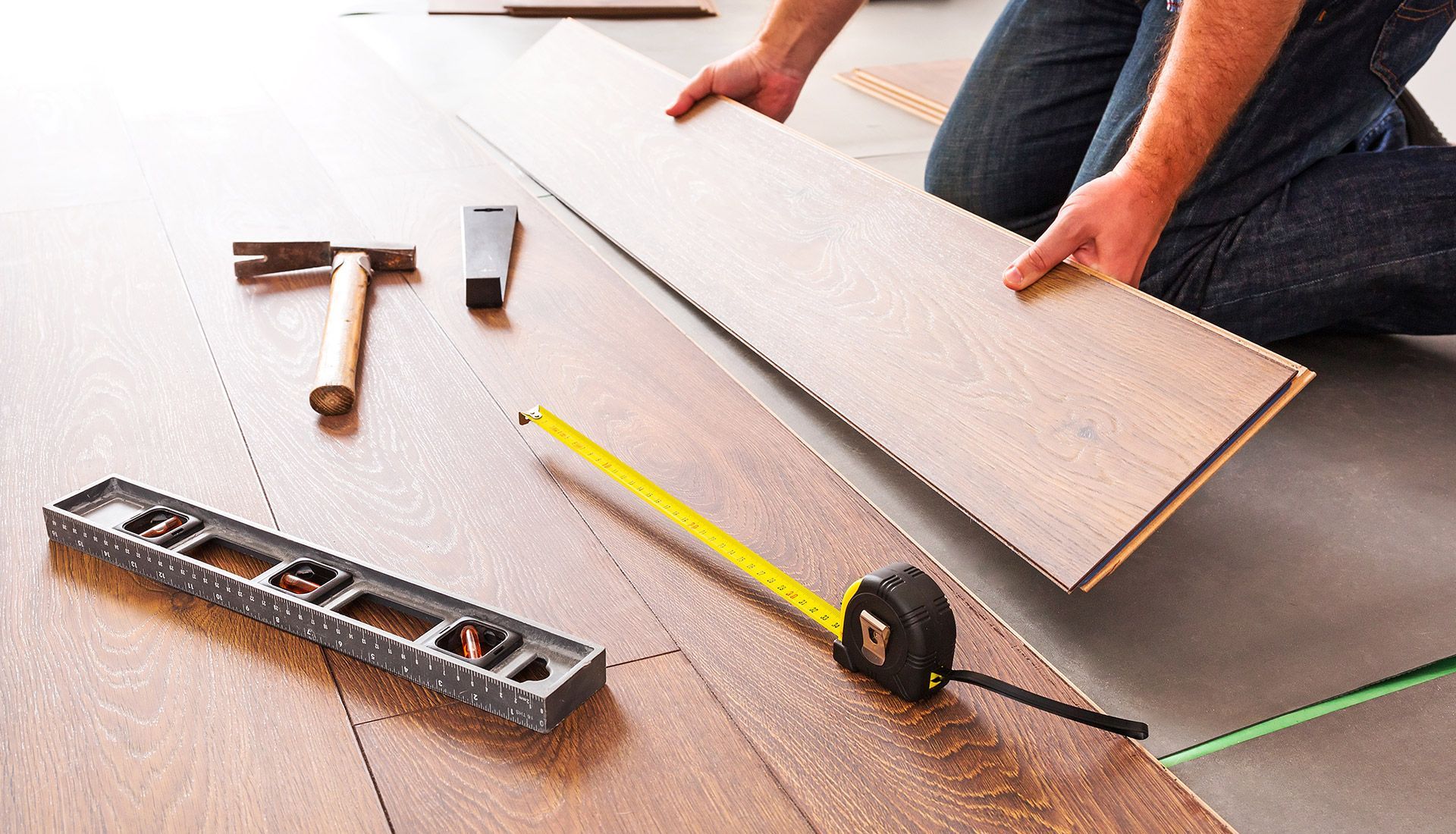 A man is kneeling down to install a wooden floor.