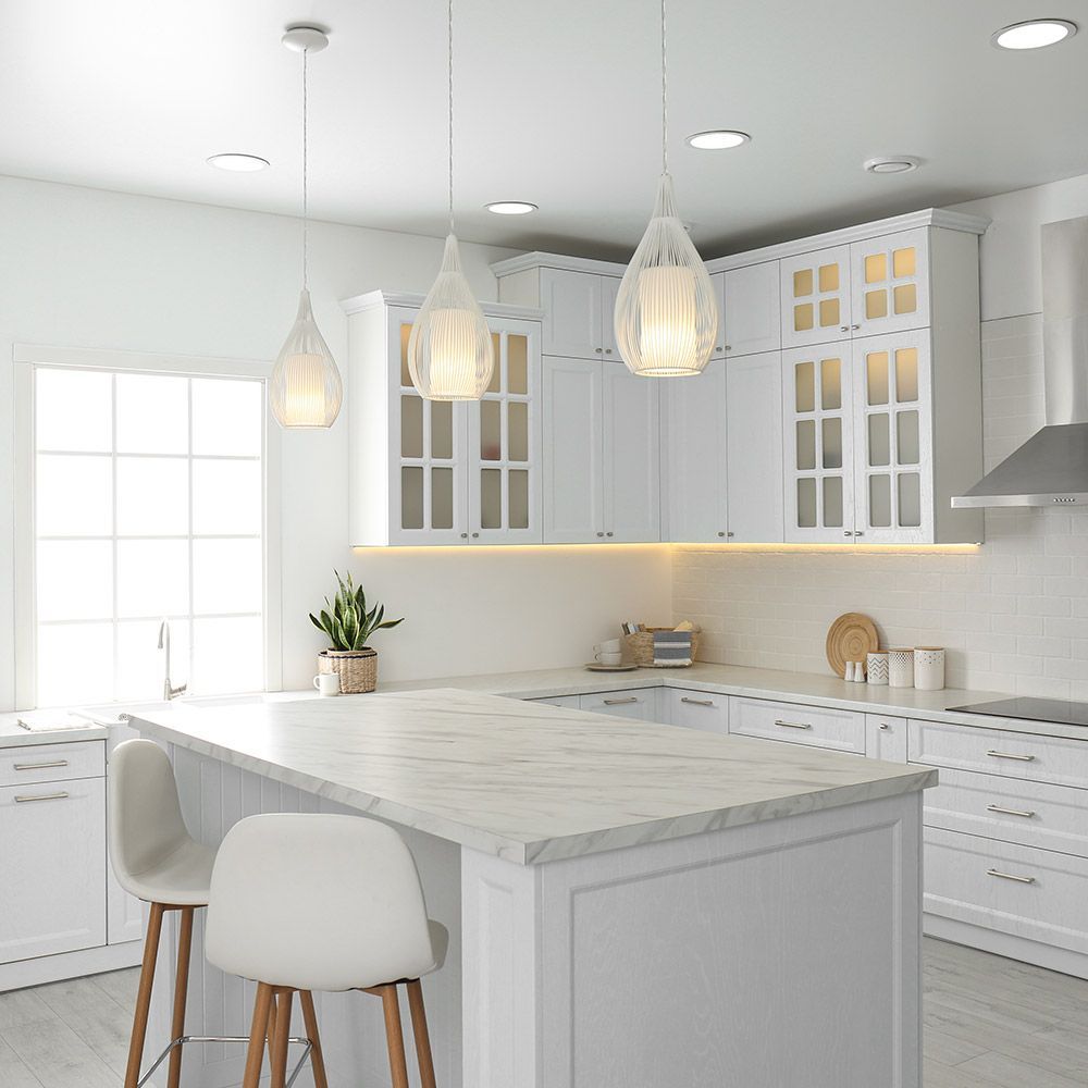 A kitchen with white cabinets , marble counter tops , stools and a large island.