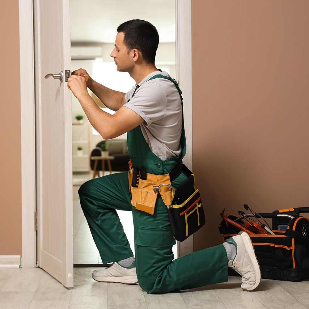 A man is kneeling down to fix a door handle.