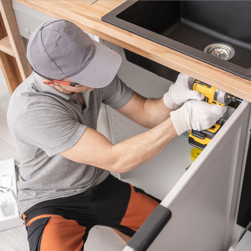 A man is fixing a kitchen sink with a drill.