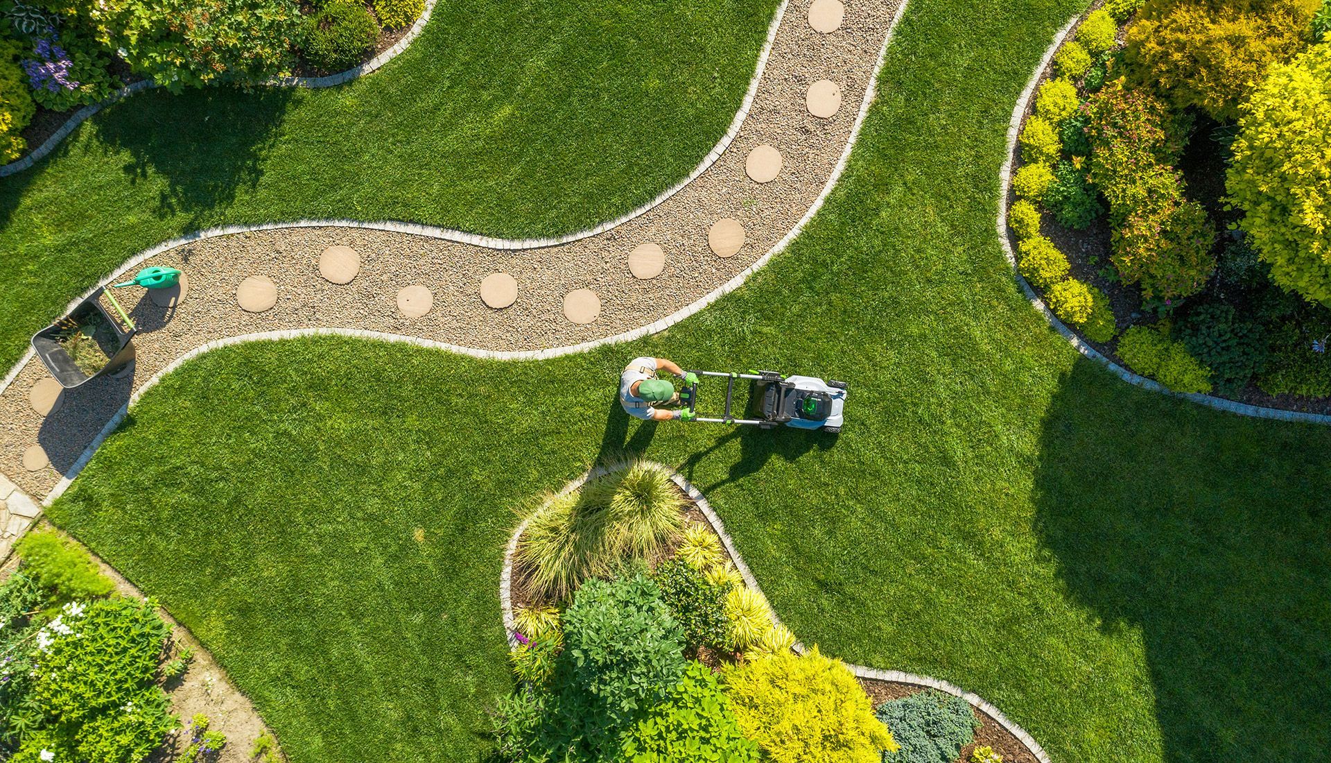 An aerial view of a person mowing a lush green lawn.