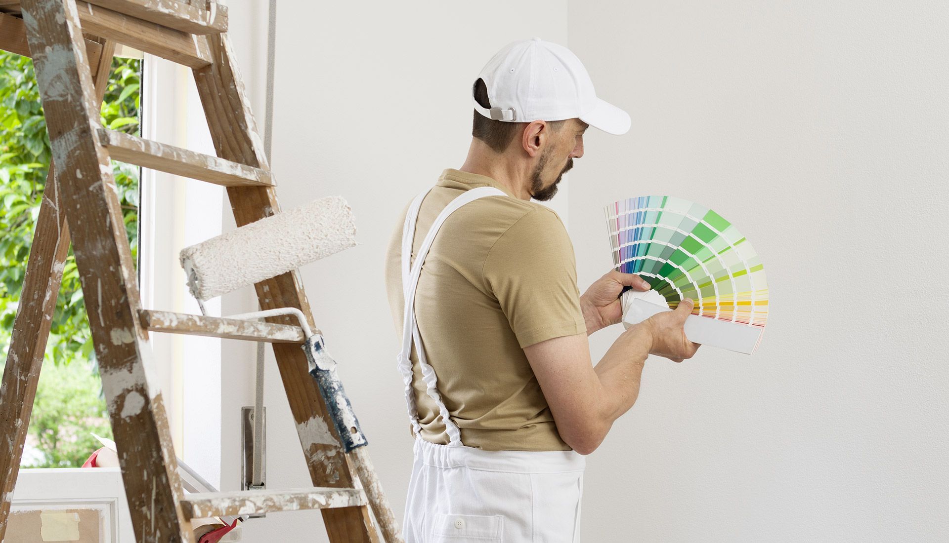 A man is standing next to a ladder holding a palette of paint.