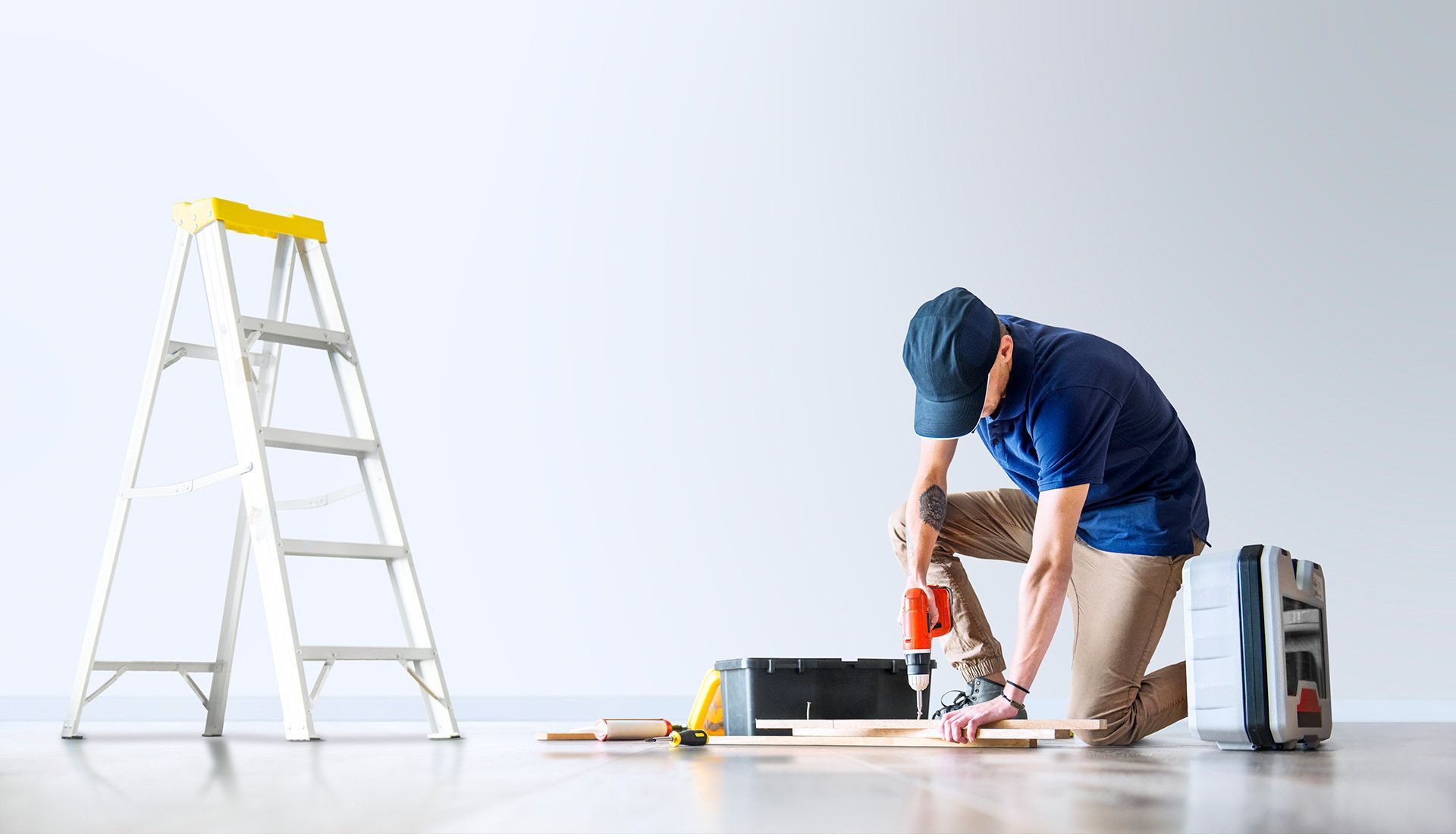 A man is kneeling on the floor using a drill.