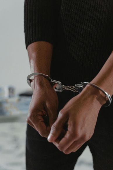 Person in a black sweater wearing handcuffs, hands clasped together.