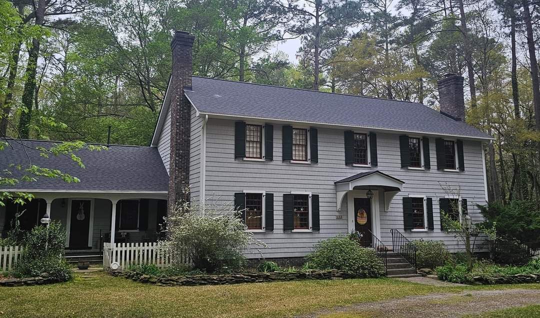 A large white house with a black roof is surrounded by trees.