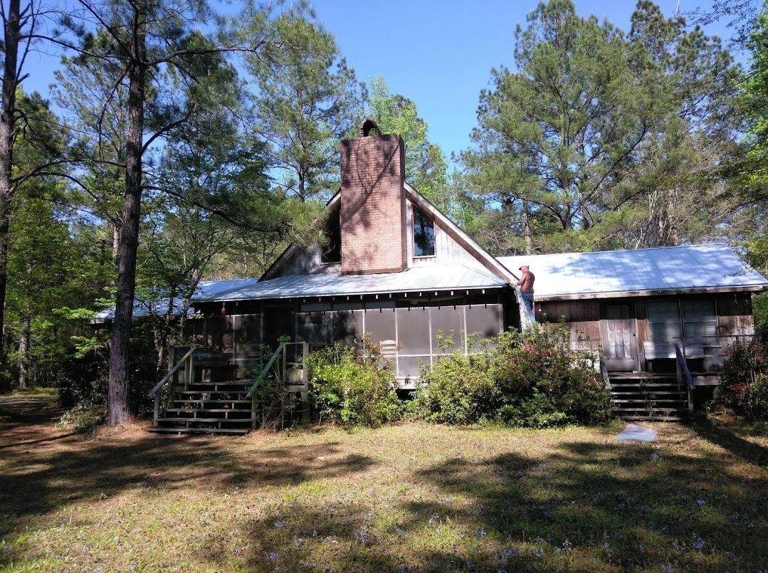 An old house with a metal roof is surrounded by trees.
