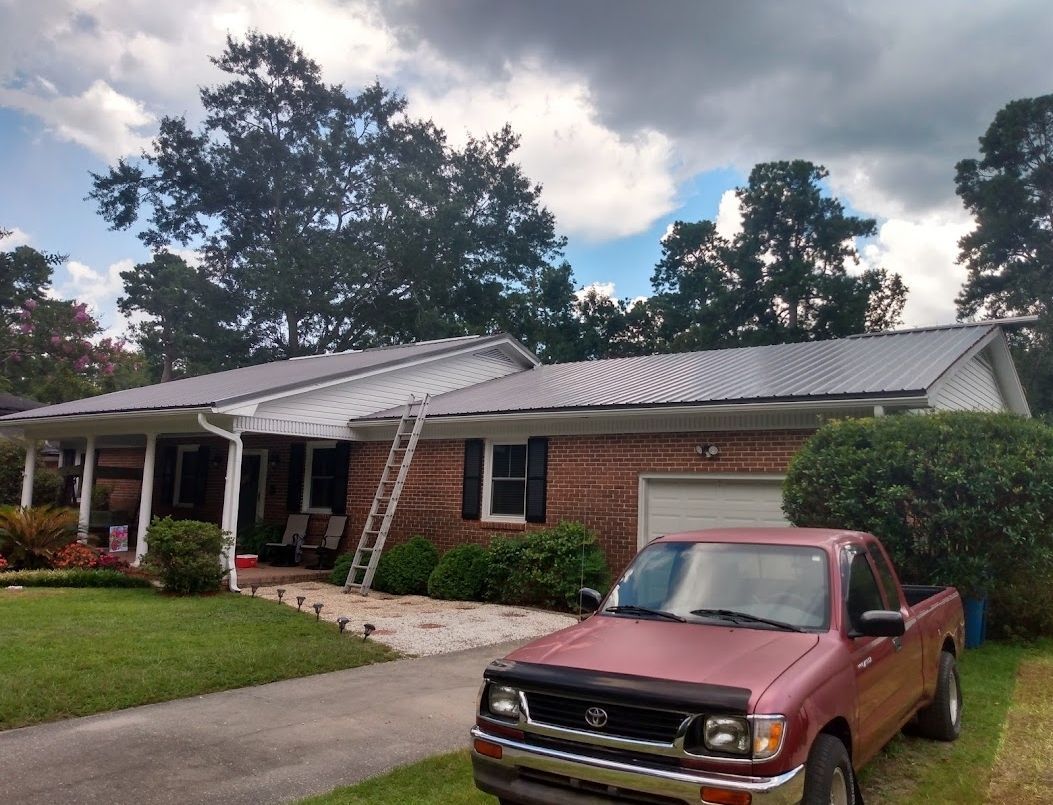 A red truck is parked in front of a brick house with a metal roof.
