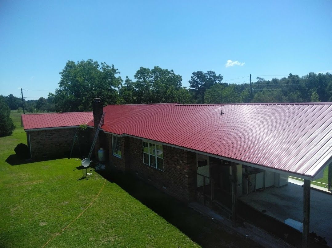A brick house with a red metal roof is sitting on top of a lush green field.