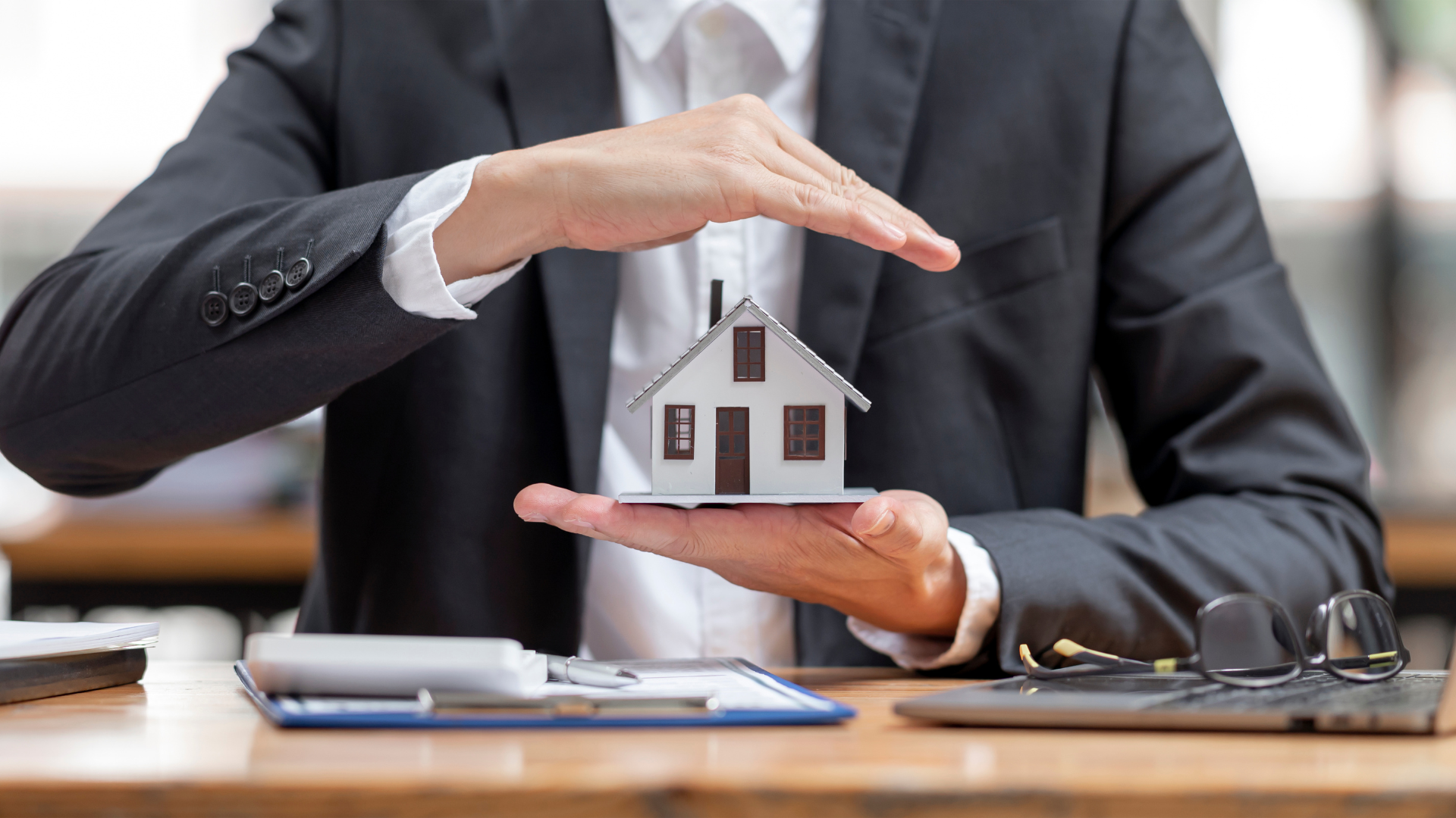 A man in a suit is holding a model house in his hands.