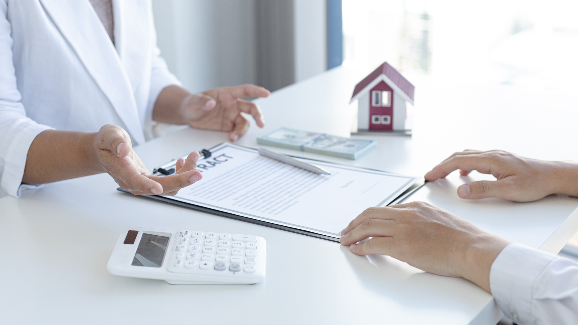 A woman is sitting at a table talking to a man about buying a house.