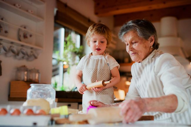 An elderly woman and a little girl are preparing food in a kitchen.