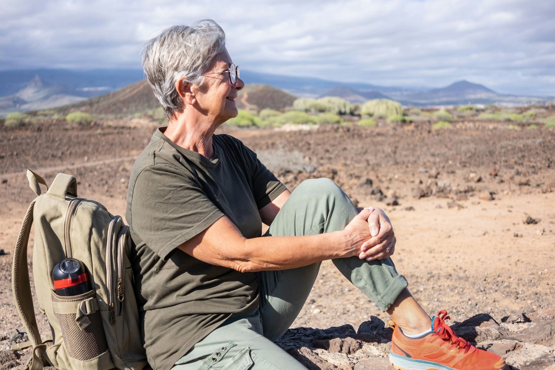 A woman is sitting on the ground in the desert with a backpack.