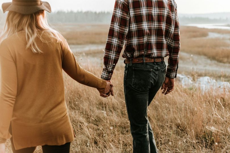 A man and a woman are holding hands while walking through a field.