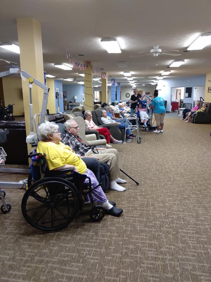 A woman in a yellow shirt is sitting in a wheelchair in a nursing home.