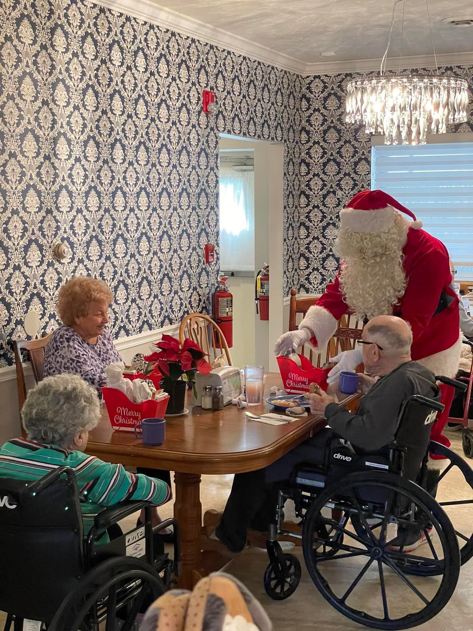 A group of elderly people in wheelchairs are sitting at a table with santa claus.
